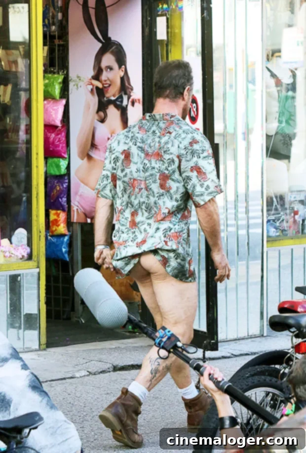 Chris Meloni, shirtless, walking down a street with only a Hawaiian shirt and boots, showing his bare backside to the camera.