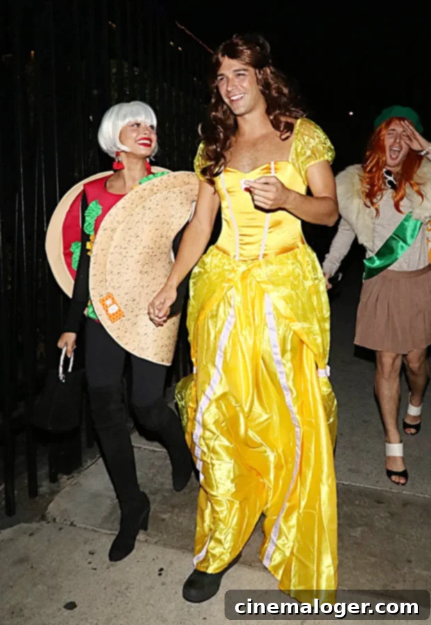 Sarah Hyland as a taco and Wells Adams as Belle in their 'Taco Belle' Halloween costume, smiling and holding hands.