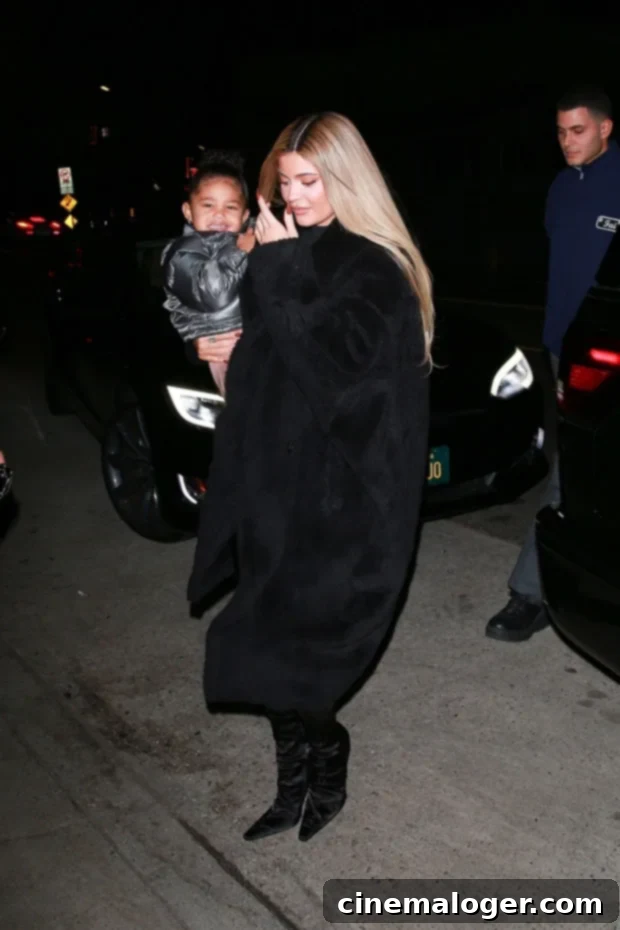 Stormi Webster smiles brightly as she is carried by her mom Kylie Jenner, both dressed in matching black outfits, during their Santa Monica outing.