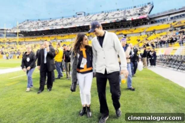 Shaggy Joins Ashton and Mila for a Cheetos Super Bowl Confession 3 Ashton Kutcher and Mila Kunis walking on an NFL sideline, a candid moment of the celebrity couple before a game.