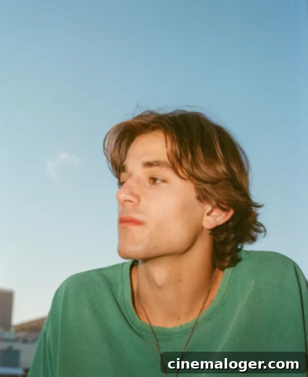 Jonah Kagen Moon His Defining Artistic Statement 2 Jonah Kagen poses for a photo, looking upwards with a gentle expression, his hand displaying a moon tattoo. The background is softly blurred, focusing attention on him.