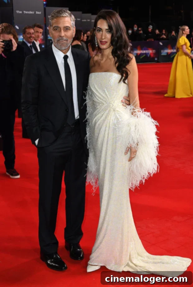 Amal Clooney Wows in Strapless Gown Alongside George at London Film Festival 2 Amal Clooney and George Clooney smiling on the red carpet at The Tender Bar premiere in London. Amal is wearing an off-white sequin gown, and George is in a black suit.