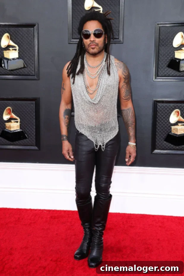 Lenny Kravitz Sparkles in Mesh Tank and Towering Heels at the Grammys 2 Lenny Kravitz poses on the 2022 Grammys red carpet in a silver mesh tank top, leather pants, and boots, showing off his tattoos.