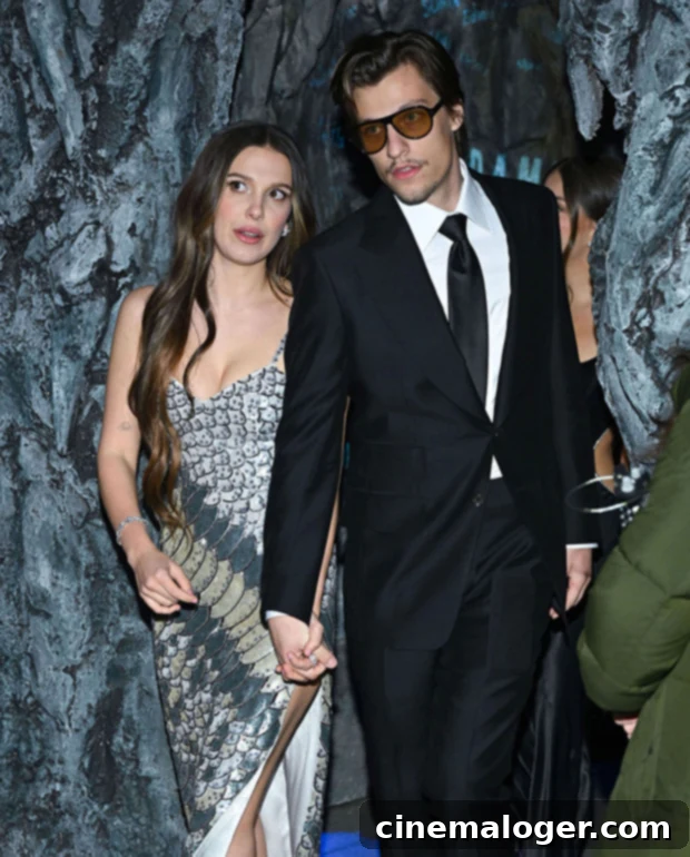 Millie Bobby Brown Debuts Wedding Band in New Get UnReady Video 2 Millie Bobby Brown and Jake Bongiovi holding hands at an event, smiling at each other.